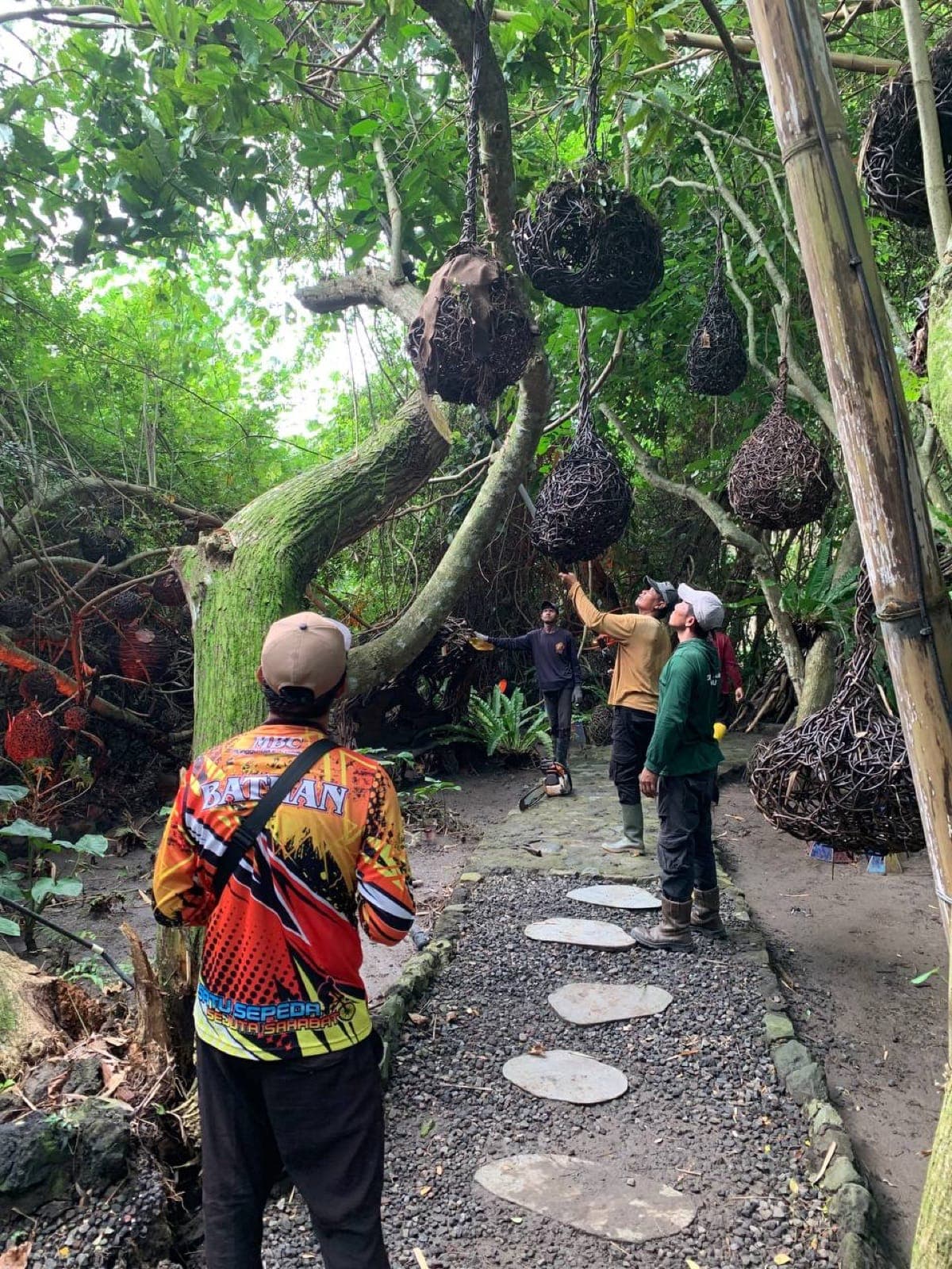 Aurora Park during commissioning — sculptural woven structures hang above a stone path, a person in a printed jacket walks ahead.