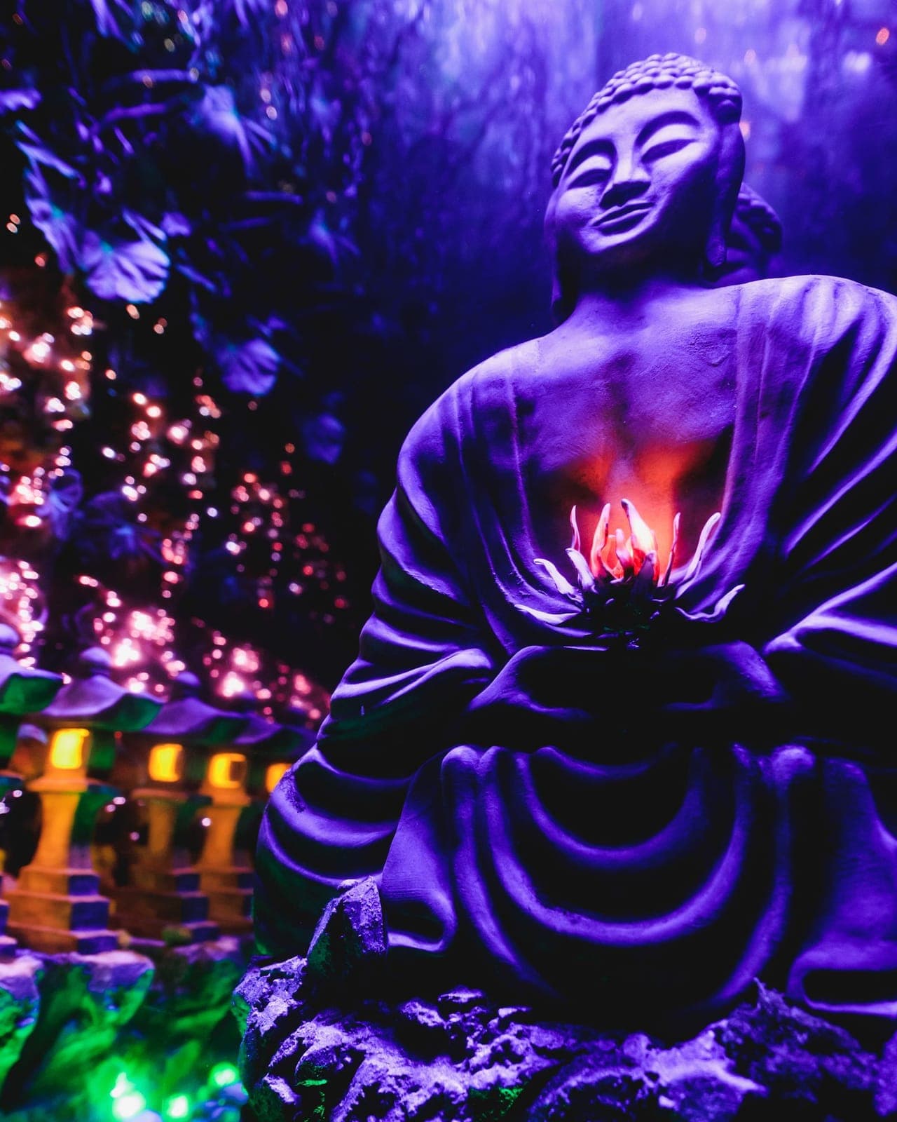 Sculpted Buddha figure holding a glowing lotus, surrounded by stone lanterns.