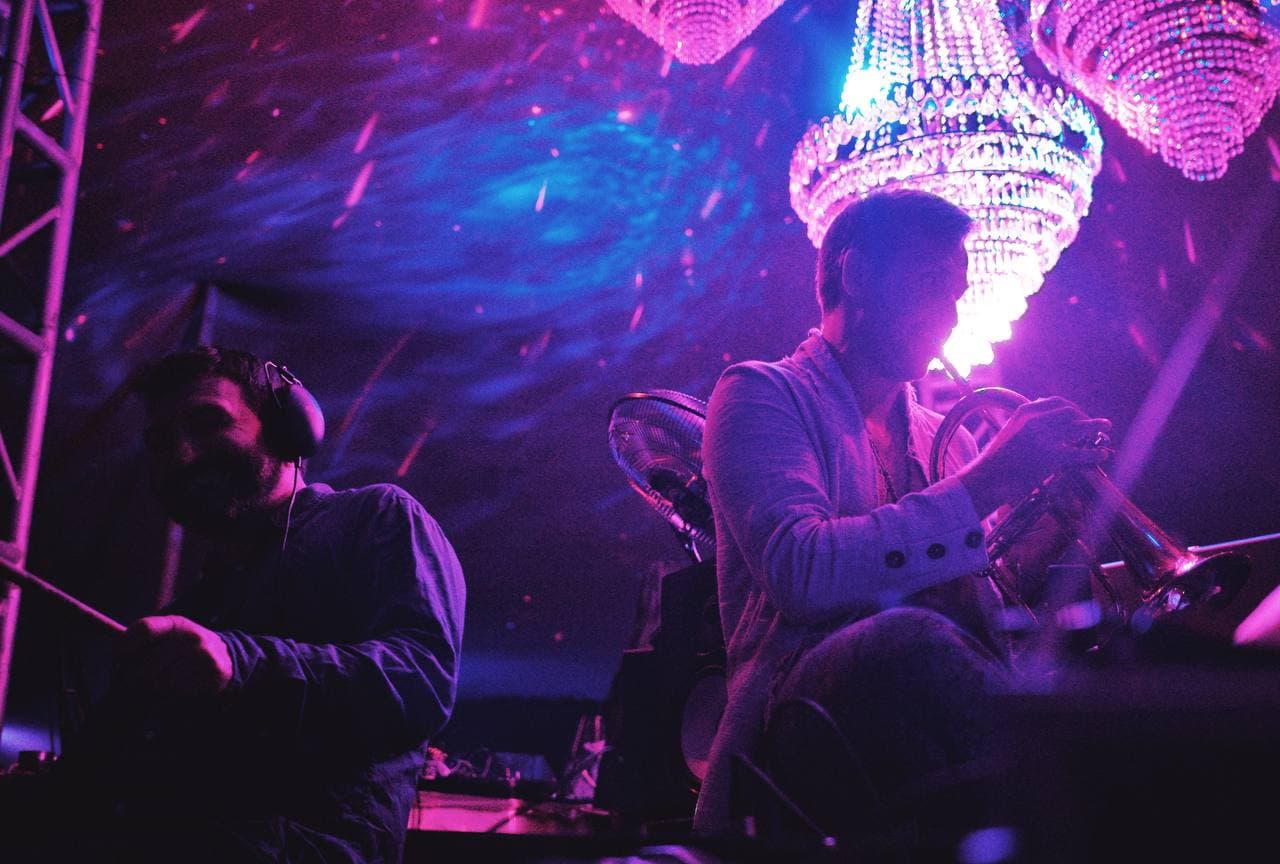 A trumpet player and electronic performer beneath the illuminated chandelier installation