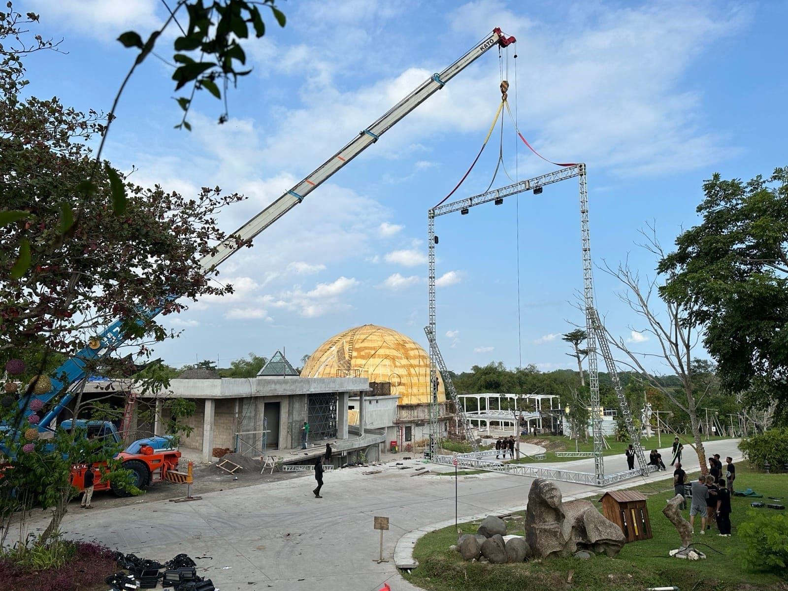 On site — a crane lifts the truss frame into position, golden dome of Nuanu's central pavilion visible behind.