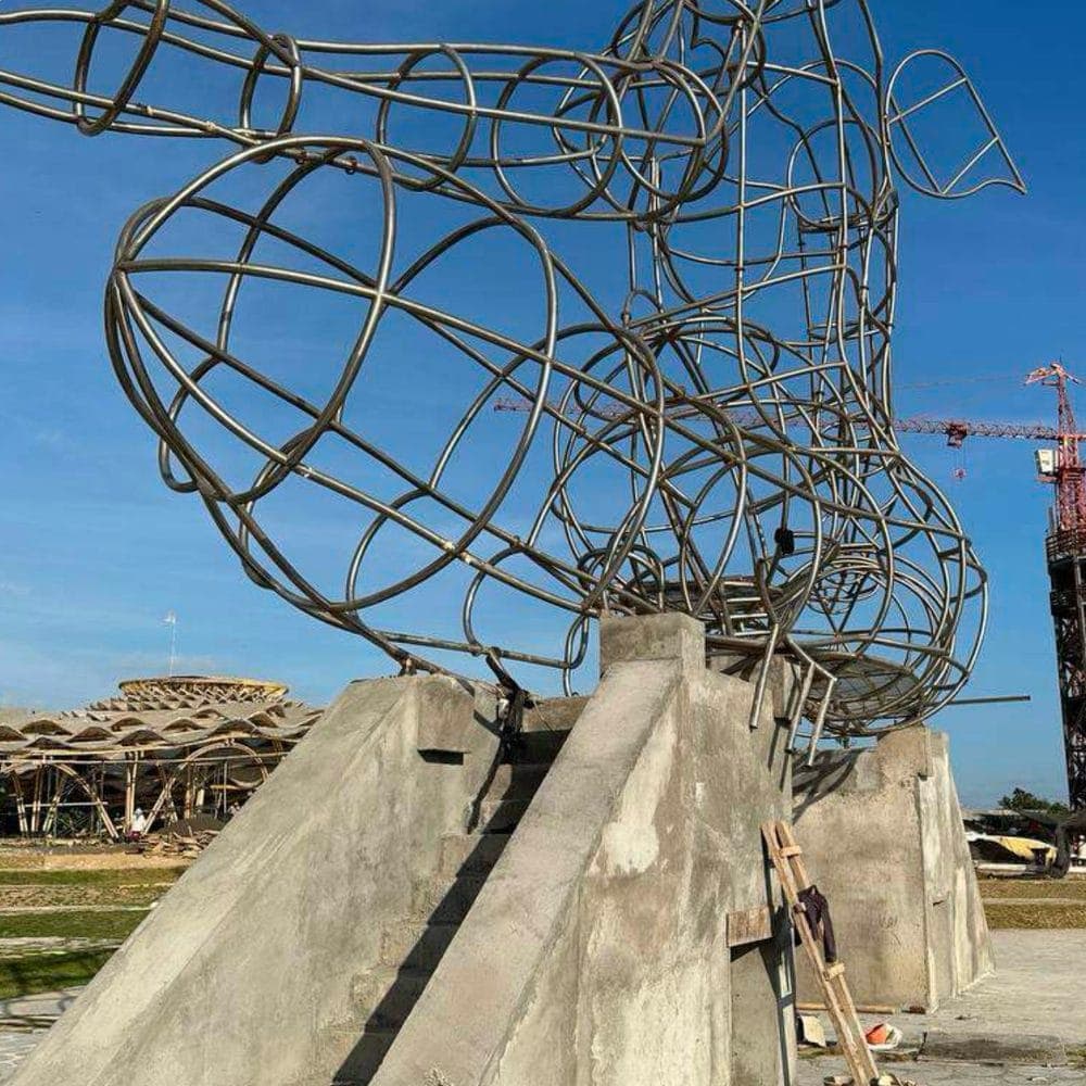 LUNA's wireframe sculpture mid-fabrication — steel armature rising from its concrete base, crane in the distance.