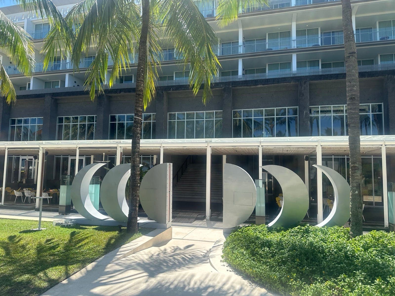 Daytime — five crescent sculptures arrayed in front of the hotel facade, palms framing the entrance.